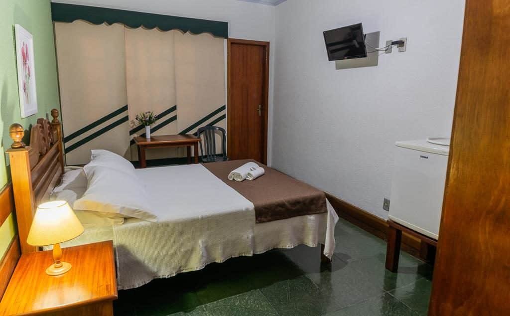 Quarto de casal da Pousada Oásis Teresópolis com tv na parede, frigobar e abajur.