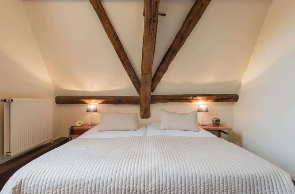 vista da cama de frente no Hotel Adornes com uma estrutura de madeira por cima e luminárias de ambos os lados