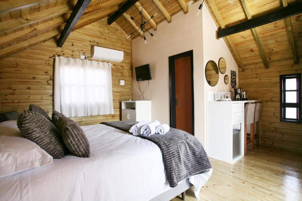 interior do chalé com uma cama de casal, um ar-condicionado, uma televisão pequena presa à parede, um balcão com duas cadeiras altas e uma área reservada para café com uma chaleira elétrica e uma cafeteira.