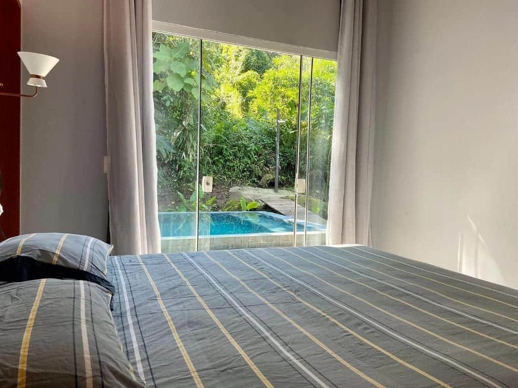 Quarto da Casa de Vidro com vista para o mar com cama de casal do lado esquerdo da imagem a frente do lado esquerdo da imagem uma porta de vidro que dá acesso a piscina. Representa airbnb em São Sebastião.