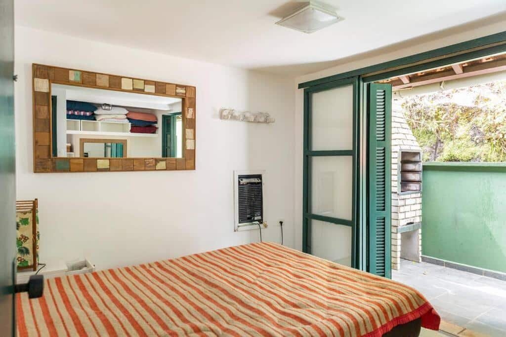 Quarto do Delba Costa Smeralda – Barra do Una com cama de casal do lado esquerdo da imagem e em frente a cama uma porta que dá acesso a varanda térrea. Representa airbnb em São Sebastião.