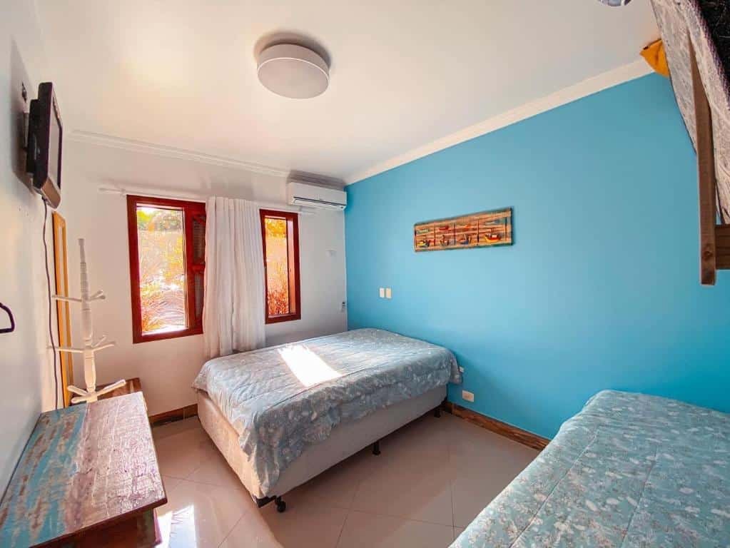 Quarto familiar do Flat Completo e Decorado em Maresias com uma cama de solteiro do lado direito da imagem do lado esquerdo do ambiente uma cama de casal, no centro do quarto uma cômoda no meio e em cima uma TV presa na parede. Representa airbnb em São Sebastião.