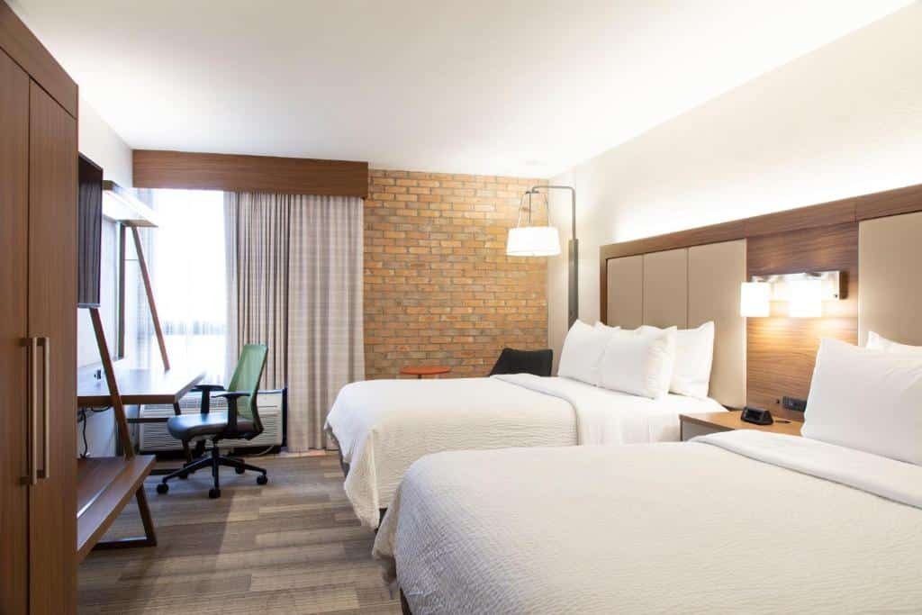 Quarto do Holiday Inn Express - San Antonio Airport, an IHG Hotel com uma cama de casal e uma de solteiro, uma parede de tijolinhos aparentes, uma janela com cortinas, um armário com duas portas, uma televisão e uma mesa de escritório com uma cadeira giratória