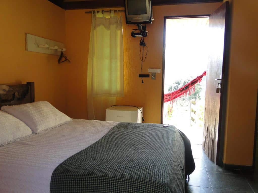 Vista do quarto com cama, TV e frigobar na  Pousada Pé da Mata.