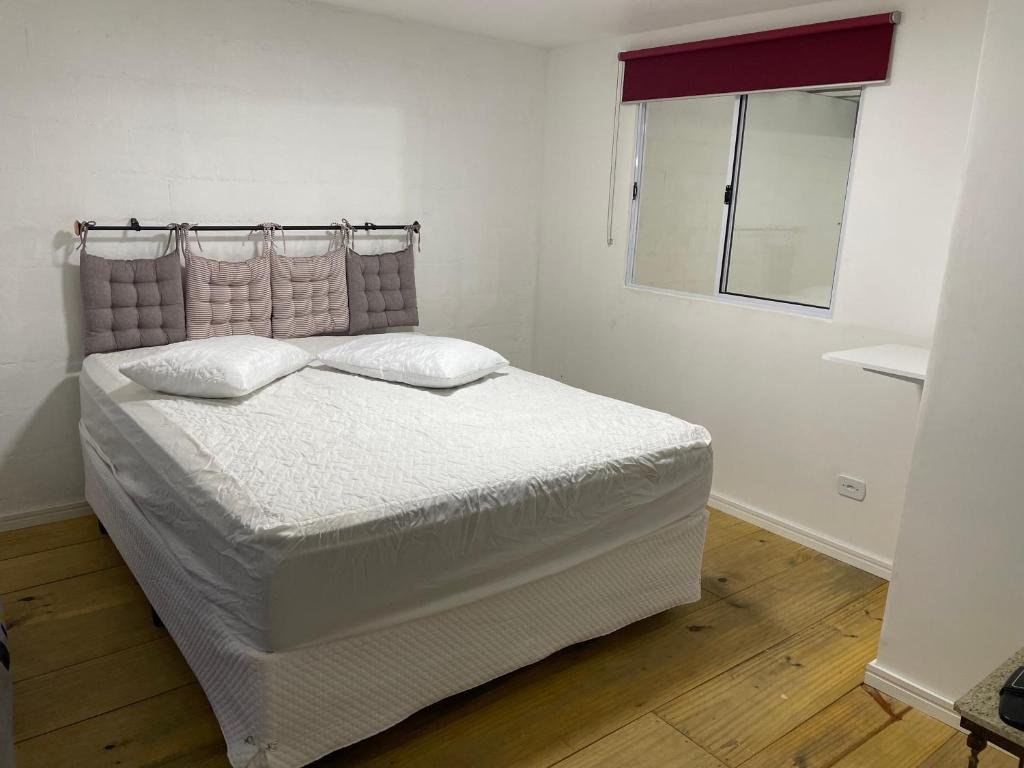 Uma cama de casal na Pousada Uchimura, com dois travesseiros em cima e almofadas de encosto. Uma janela no canto direito.