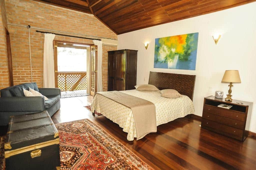 Quarto na Locanda Buona Fortuna. Um baú e uma poltrona no canto esquerdo. No canto direito uma cômoda, uma cama de casal e um guarda-roupa. No fundo a porta da sacada.