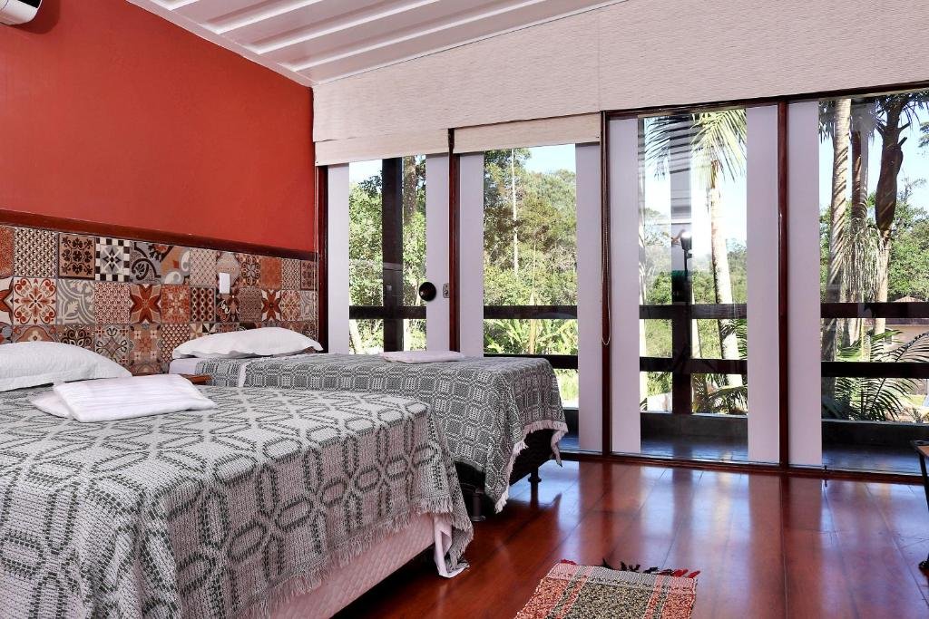 Quarto na Pousada Vale do Sol. Duas cama de casal do lado esquerdo. A parede com portas de vidro e acesso a sacada.