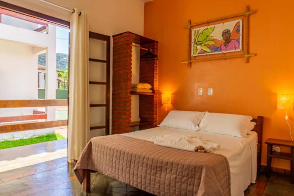 Quarto da Pousada Casarão com cama de casal do lado direito da imagem no centro do quarto e do lado esquerdo da cama uma cômoda de madeira.