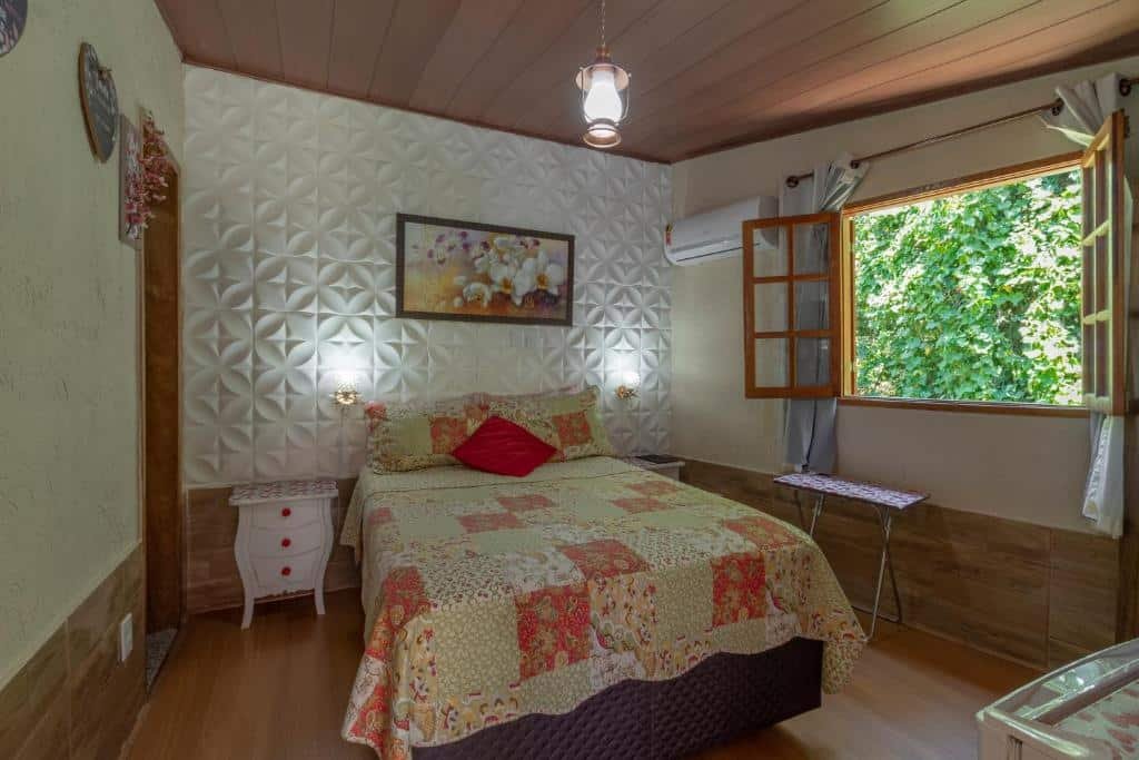 Quarto da pousada cascata dos amores em Teresópolis com cama de casal e janela aberta mostrando a paisagem. 