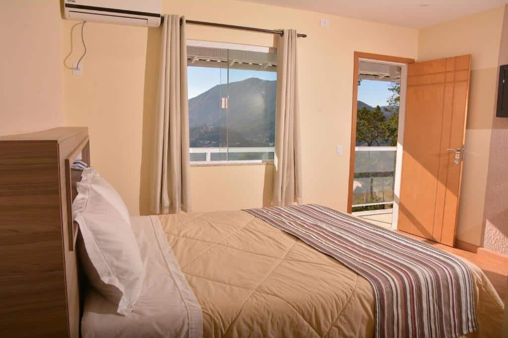 Quarto da pousada in garden em Teresópolis bem iluminado com uma cama de casal, janela de vidro e porta de madeira, post ilustrando pousadas em Teresópolis.