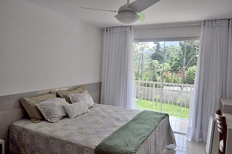 Quarto da pousada Matitaterê em Teresópolis com cama de casal, portas de vidro com vista para a varanda e cortinas brancas, ilustrando post pousadas em Teresópolis.