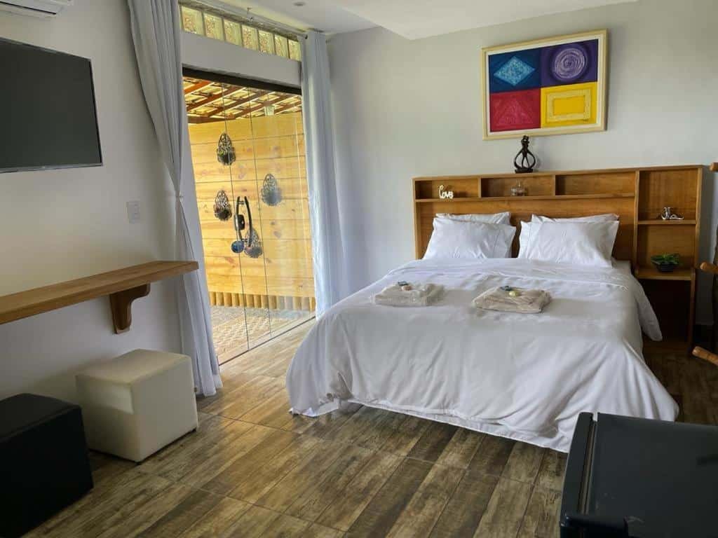 Quarto da pousada r.n.c nosso paraíso em Teresópolis com cama de casal, tv na parede e porta de vidro.