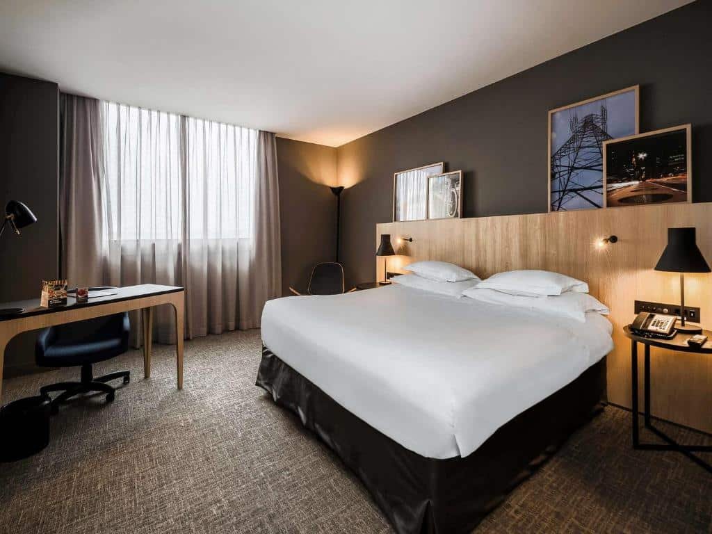 Quarto preto e branco no Pullman Sao Paulo Guarulhos Airport. Uma cama de casal no lado direito com iluminarias. No canto esquerdo uma mesa de trabalho.