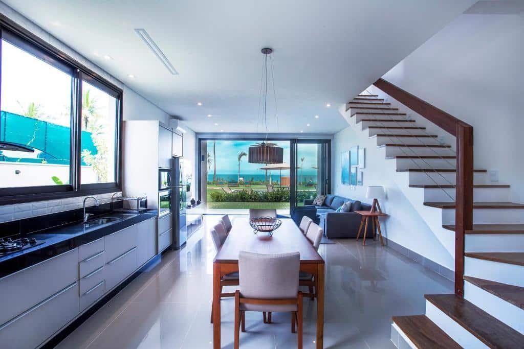 Cozinha e sala no Residencial Marina Del Sol. A cozinha é espaçosa, há uma mesa de jantar no centro, uma escada na direita e pia à esquerda. A sala está no fundo. Representa airbnb em São Sebastião.