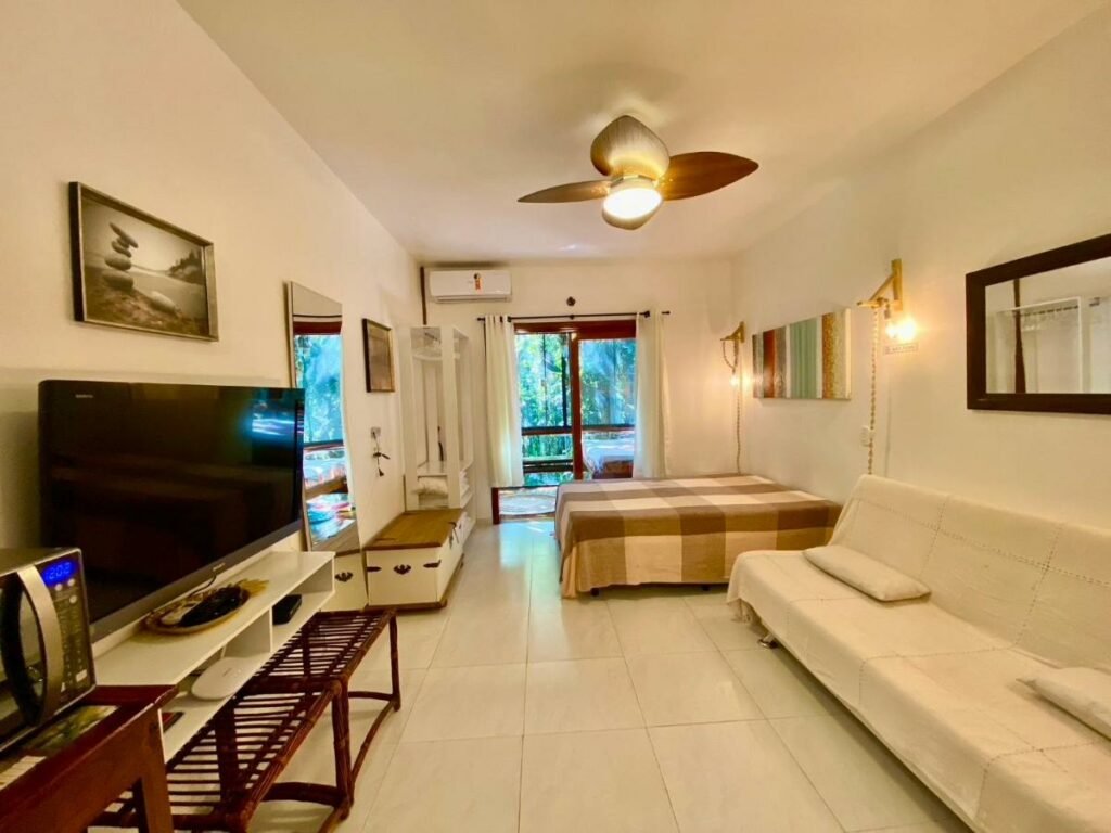 Sala de estar do Housing 31 com sofá do lado direito da imagem a frente e em frente uma cômoda com TV, do lado direito do sofá uma cama de casal.