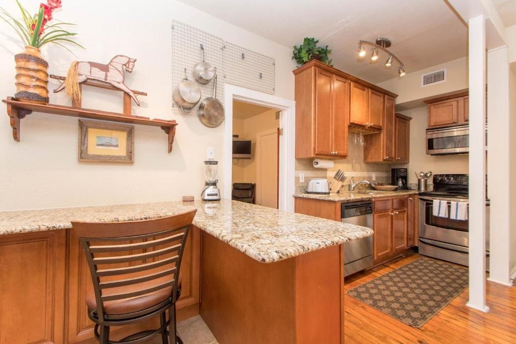 Cozinha do THE MADISON - San Antonio Riverwalk - Downtown - Convention Center com fogão, lava-louças e utensílios gerais, há uma bancada com uma cadeira e alguns itens de decoração em madeira