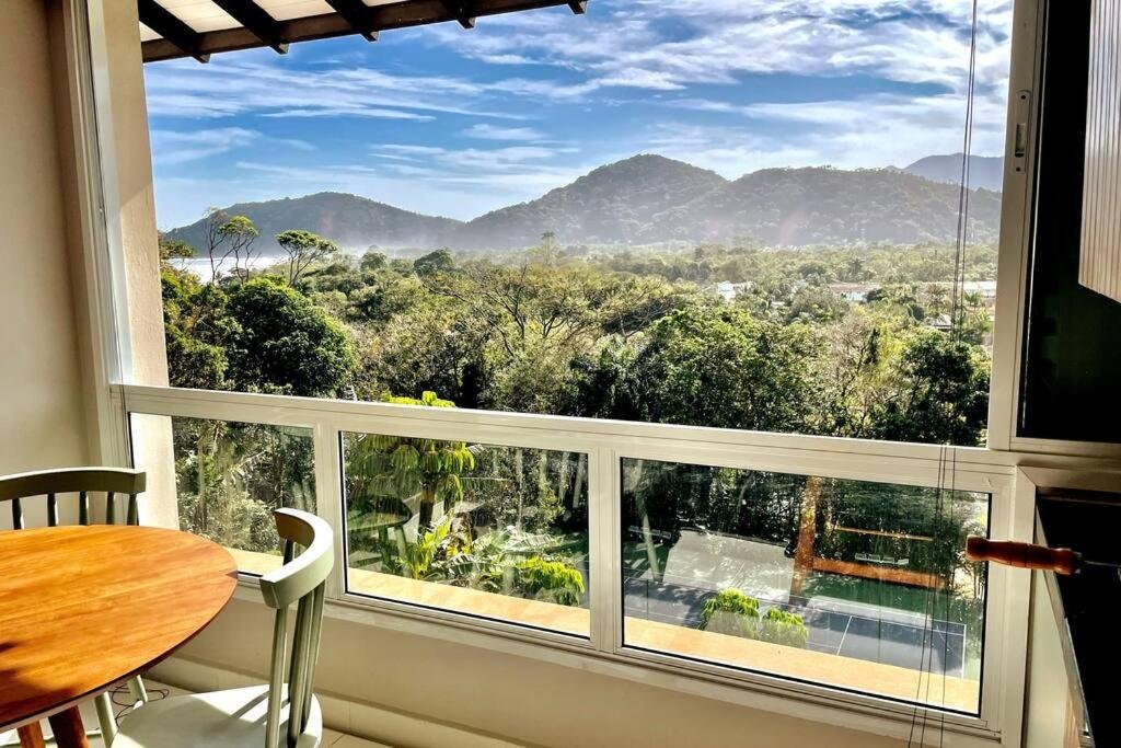 Varanda do Camburizinho 3 suítes aconchegante durante o dia com mesa do lado esquerdo da imagem com vista para as montanhas.